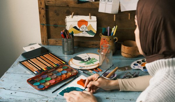 person painting with paintbrush, art supplies surrounding them on table